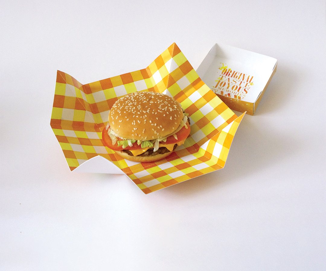 Burger set on checked greaseproof paper inside a board tray