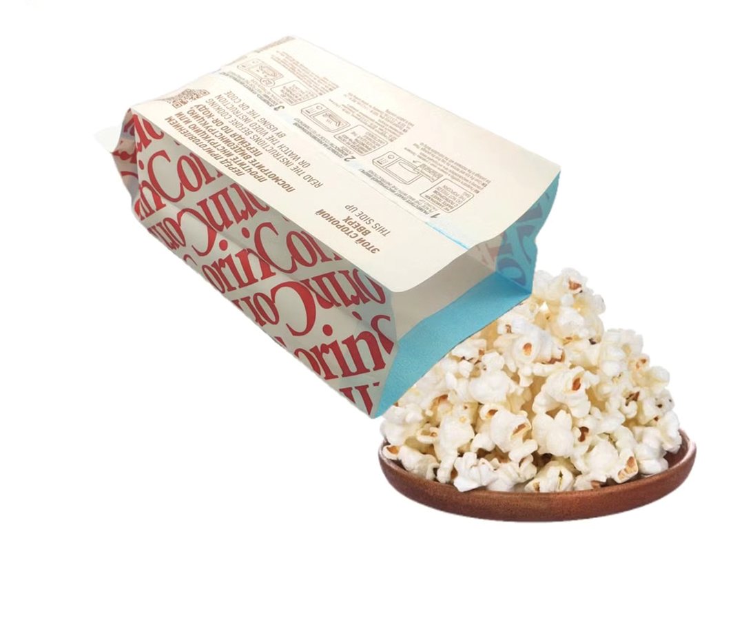 Printed popcorn carton laid on its side beside a plate of popcorn