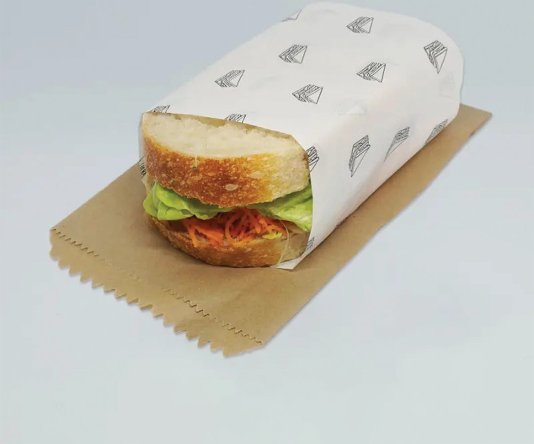 Sandwich wrapped in printed paper and set on a kraft board base