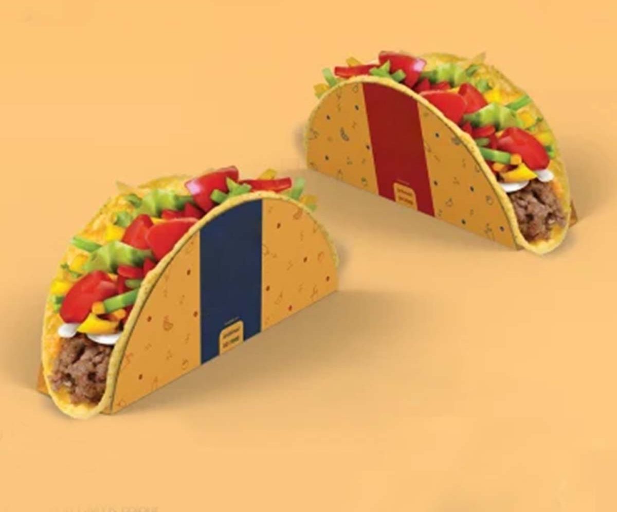 Two filled tacos held in printed board sleeves on an orange backdrop